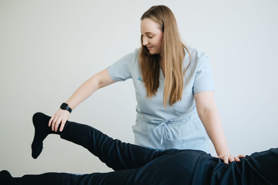 Female physiotherapist assisting patient in leg therapy session. Indoor clinical setting.