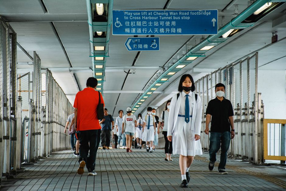 People crossing Cheong Wan Road footbridge in Hong Kong with school uniforms and urban signage.