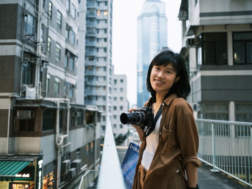 Smiling woman photographer holding camera on a street in Hong Kong.