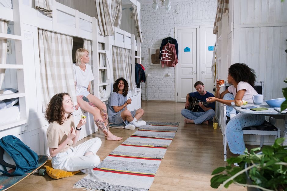 A diverse group of friends enjoying leisure time in a cozy shared dorm room with bunk beds.
