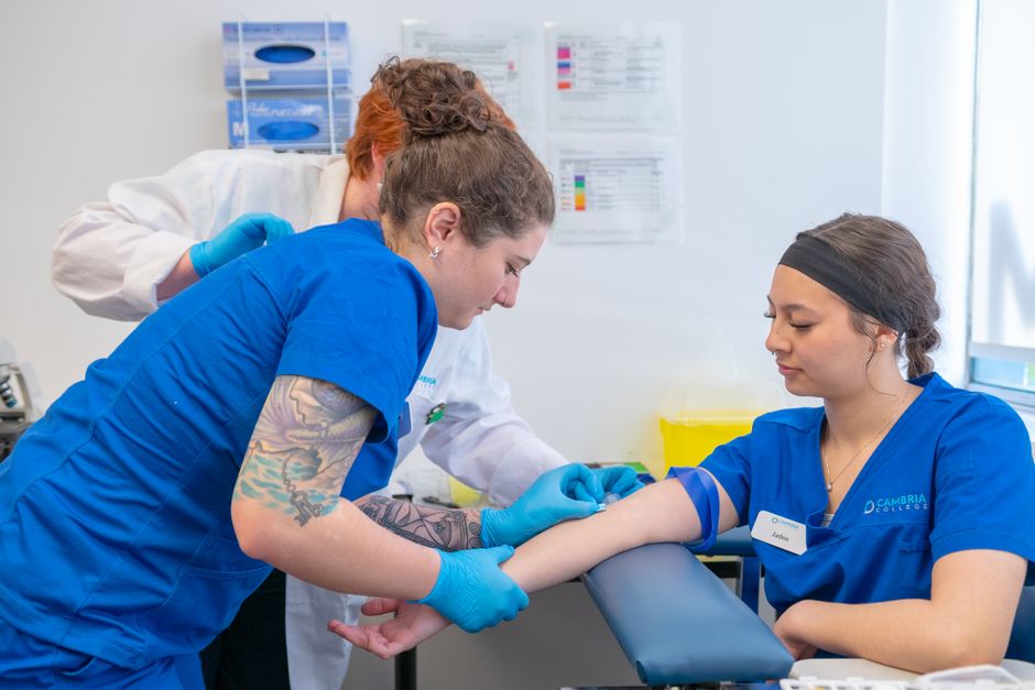 Nurses and a medical student practice blood draw in a clinical setting.