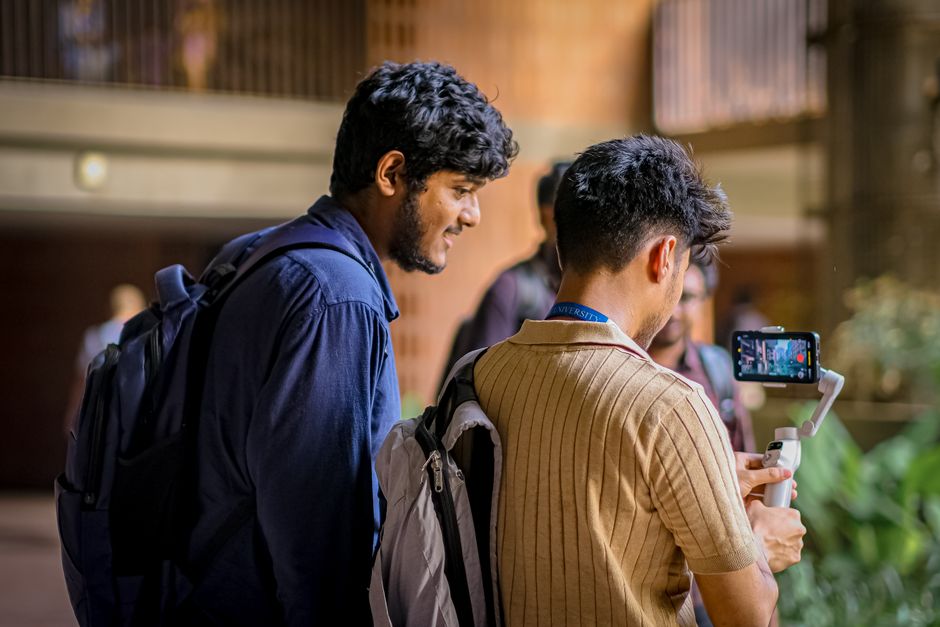 Two students capturing video content using a mobile stabilizer indoors at a university.