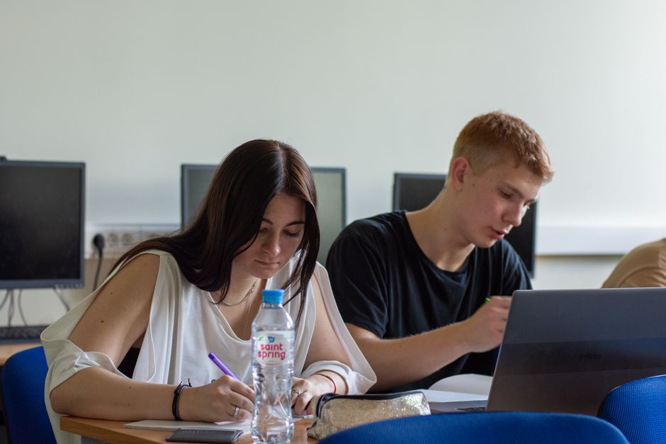 Two students focused on studying in a computer lab, using a laptop and taking notes.