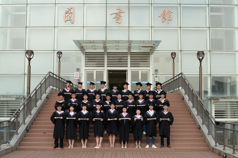 Group of graduates in academic dress standing on stairs, celebrating their achievement.