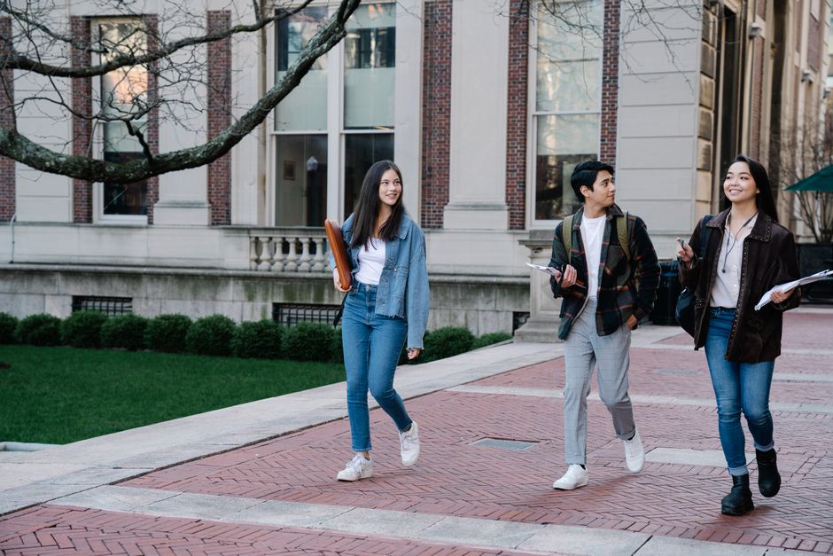 Group of young students walking on campus sidewalk on a bright day, showcasing casual university life.