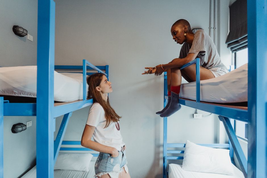 Two women engaging in conversation on bunk beds in a modern dormitory room.