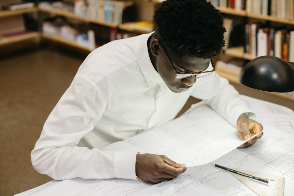 Young man intensely studying architectural blueprints in a library setting.