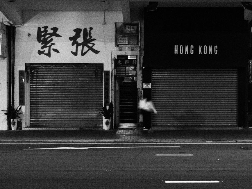 Moody black and white photo capturing a quiet Hong Kong street with closed shopfronts.