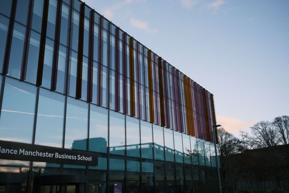 Modern architecture of Alliance Manchester Business School reflecting in glass facade at dusk.