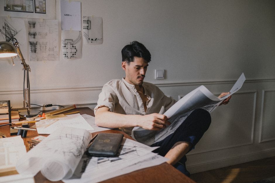 Man reviewing architectural plans at desk in sunlight, displaying concentration and creativity.