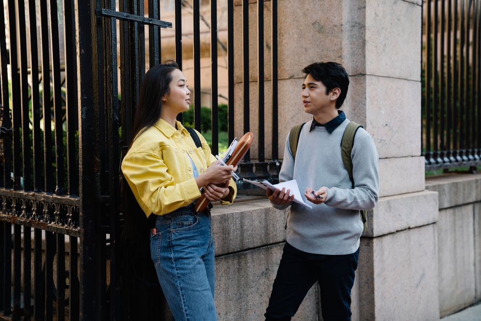 Two young adults engaged in conversation near a university gate.