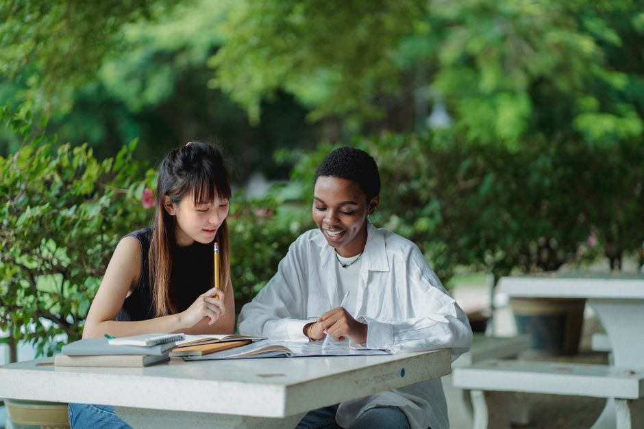 Cheerful African American and Asian female students sitting at table and doing research together